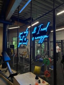 Blue handwritten LED neon slogan sign on a gym glass wall
