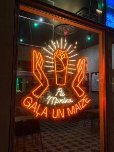 Orange LED neon shop window sign "Gaļa un maize" with hands and a sandwich