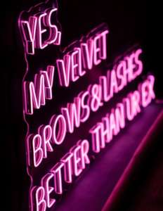 Pink LED neon sign "Yes, my velvet brows & lashes" in a beauty salon