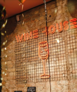 Orange "Wine House" LED neon sign with a wine glass on a metal grid