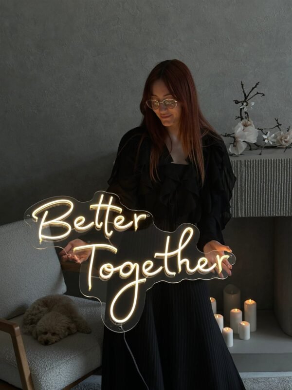 Woman holding a warm white Better Together LED neon sign with candles
