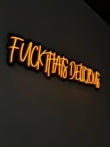 Orange handwritten LED neon slogan sign on a dark restaurant wall